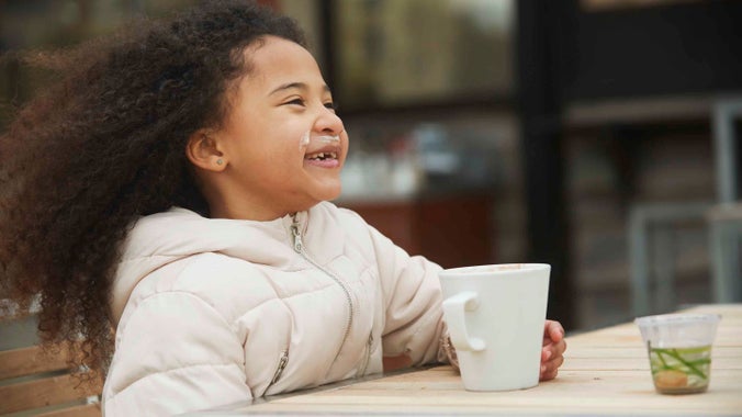 A close-up of a smiling child enjoying a cut of hot chocolate at Knoll Beach café, Studland Bay